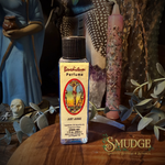 A bottle of 'Just Judge' perfume by Baphometian Perfume is displayed on a wooden surface surrounded by mystical props including a pink crystal candle, a blue robe figurine, and dried botanicals. The Smudge Spiritual Boutique & Botanica logo is visible in the bottom right corner.
