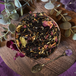 Tea leaves in a wooden bowl with eucalyptus leaves and amethyst crystals on a purple fabric background