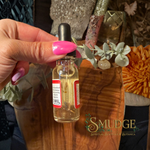 A hand with bright pink nails holds a small glass dropper bottle containing a golden liquid. The bottle has a black dropper cap and red-and-white labels.