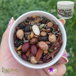 Hand holding a bowl of mixed seeds with a container labeled 'Granos Magnetico' in the background.