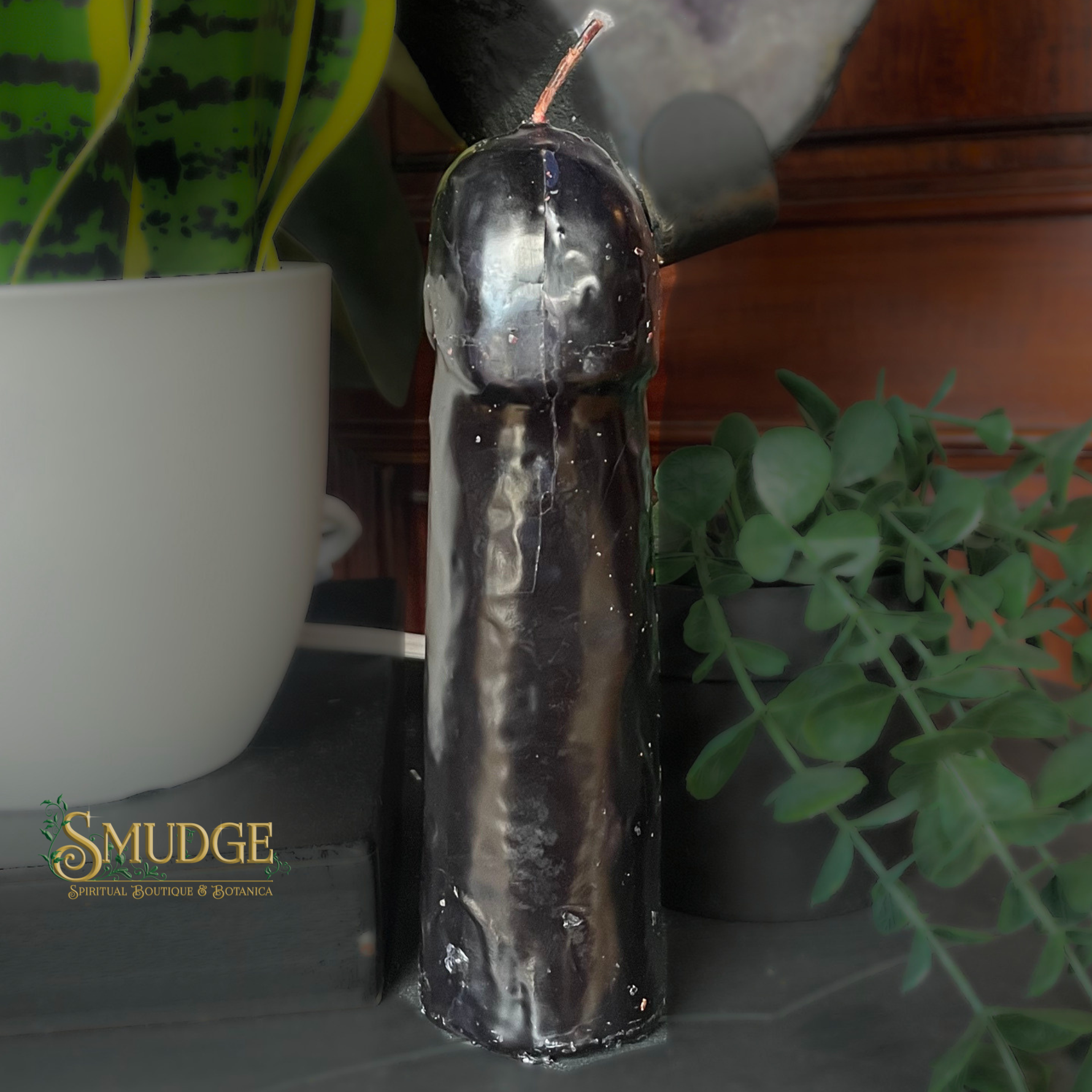 Decorative candle with metallic finish on a surface with plants in the background, featuring the brand 'Smudge'.