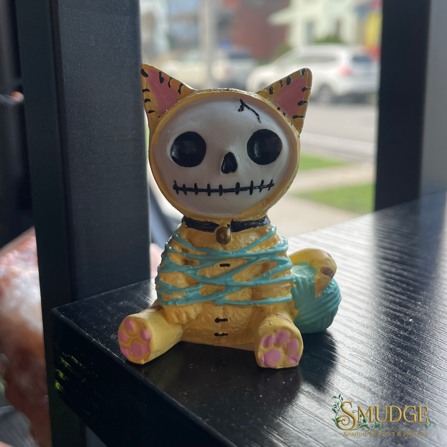 Skull-shaped cat figurine with colorful mummy bandage on a reflective surface