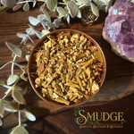 A bowl of chopped, dried mistletoe european on a wooden background with eucalyptus and an amethyst crystal beside it. 