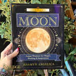 A hand holds the front cover of the book 'Llewellyn's Complete Book of the Moon' by Jesamyn Angelica. The cover features a large golden moon on a dark starry background with gold and blue text.