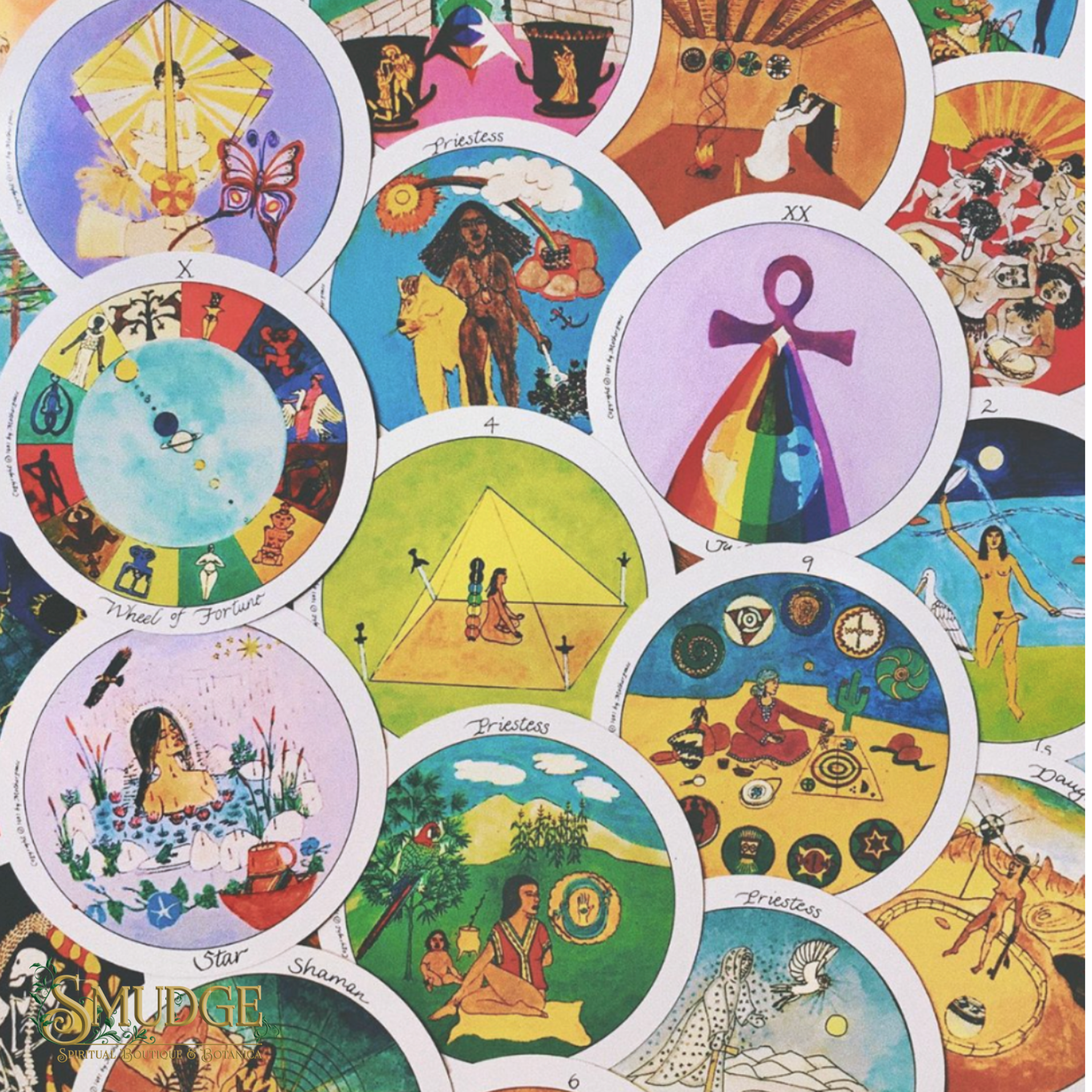 A close-up of a printed textile or patchwork surface featuring multiple overlapping circular illustrations in bright, varied colors. The design includes symbolic and spiritual motifs such as a butterfly, a rainbow ankh symbol, a pyramid, a bird, a face, and other abstract scenes.