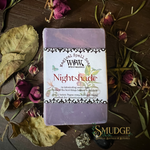 A rectangular bar of lavender soap labeled 'Witchy Spell Soap' and 'Nightshade' by WWC, placed on a dark wooden surface surrounded by dried leaves, petals, and green stems. A 'SMUDGE' brand mark appears in the lower right corner.