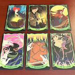 Six illustrated oracle cards arranged in two rows on a reddish-brown wooden surface. The cards feature fantasy artwork with green borders and titles including The Magician, The Fool, The Chariot, The Transformation, The Hermit, and The High Priestess.