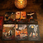 Six illustrated tarot or oracle cards arranged on a wooden tabletop, with a lit candle above them. The cards feature autumn and mystical scenes with text such as 'Crazy maple,' 'Maple tree,' 'Your dreamable,' 'Harvest witch,' 'Pumpkin spice and apple cider,' and 'Crazy fire.