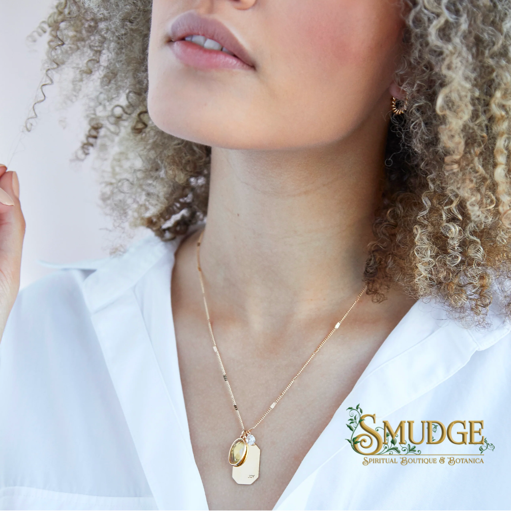 A close-up lifestyle shot of a model wearing a delicate gold necklace with two interlocking oval pendants, one engraved with 'LOVE'. The model has curly blonde hair and is wearing a white collared shirt.