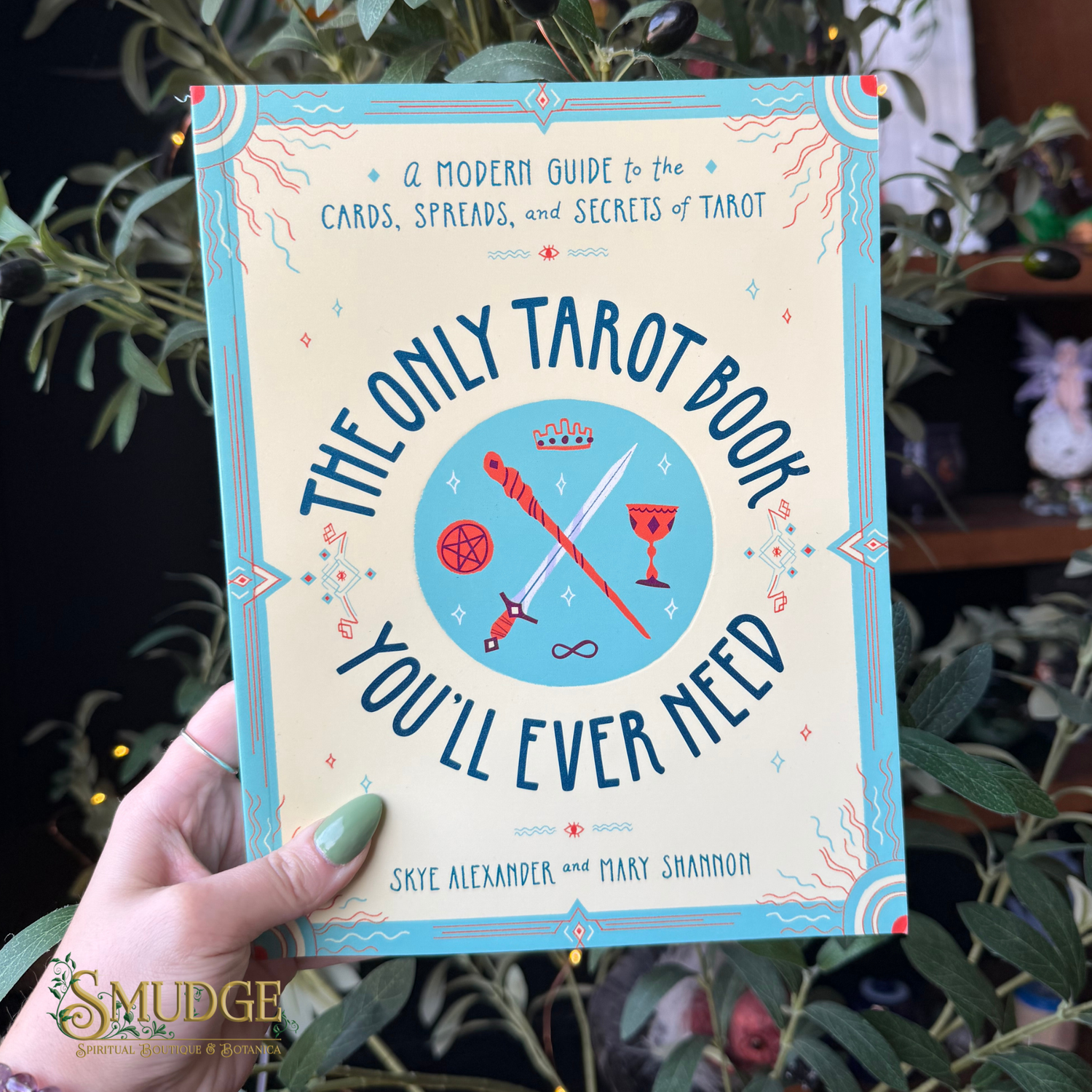 A hand holds a book titled 'The Only Tarot Book You'll Ever Need' by Skye Alexander and Mary Shannon. The book has a cream cover with a light blue border and colorful tarot card illustrations.