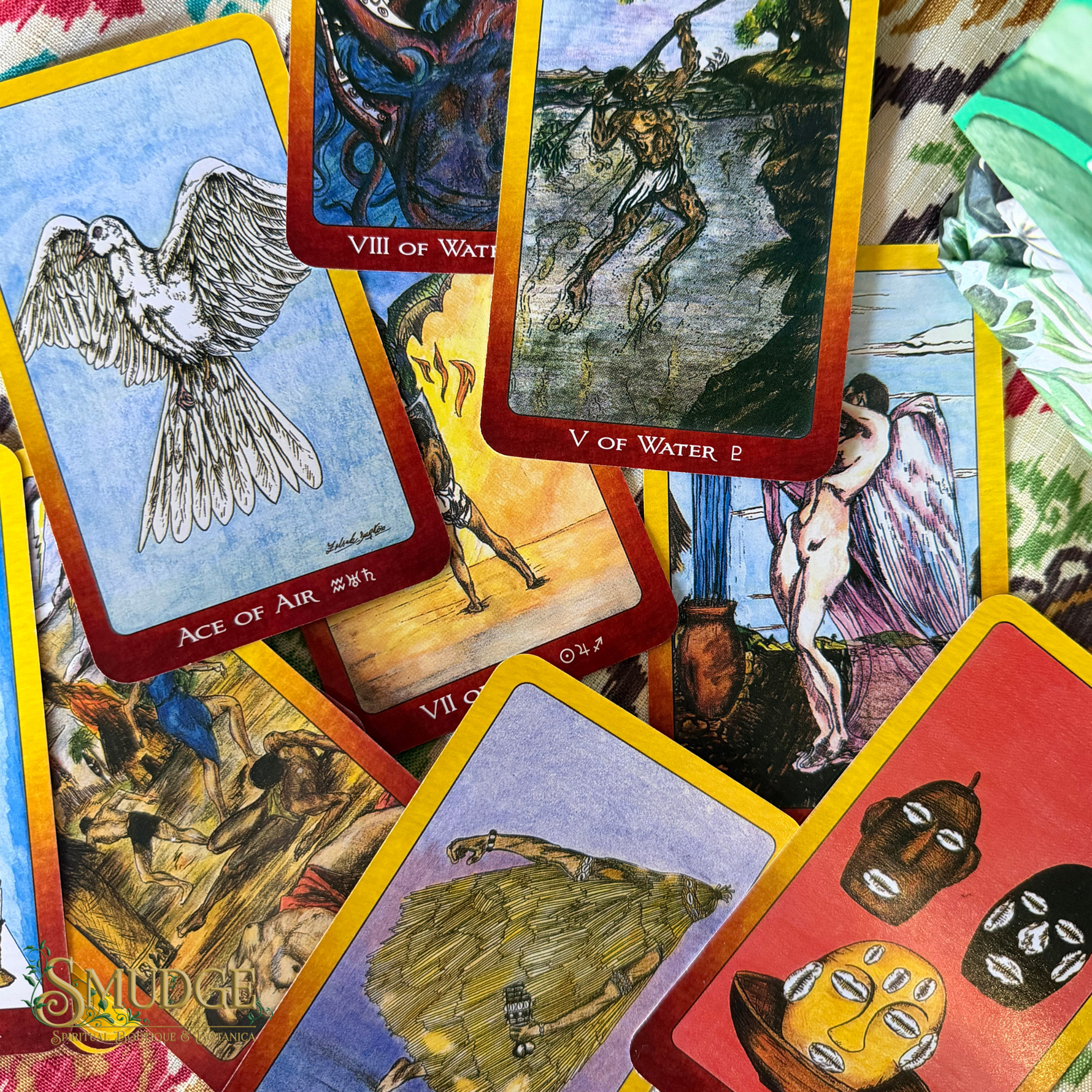 A spread of illustrated tarot-style cards with red borders and yellow edges, including visible titles such as Ace of Air, VIII of Water, V of Water, and others, photographed on a patterned fabric background.
