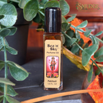 A bottle of Sea 'n Sky Patchouli perfume oil with a black cap and beige label, set on a dark surface with green leaves and orange autumn leaves in the background.
