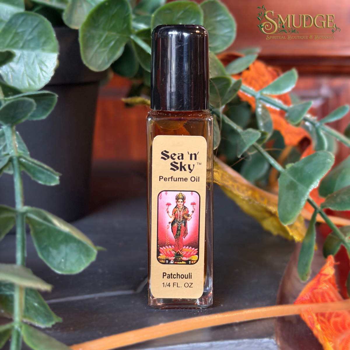 A bottle of Sea 'n Sky Patchouli perfume oil with a black cap and beige label, set on a dark surface with green leaves and orange autumn leaves in the background.