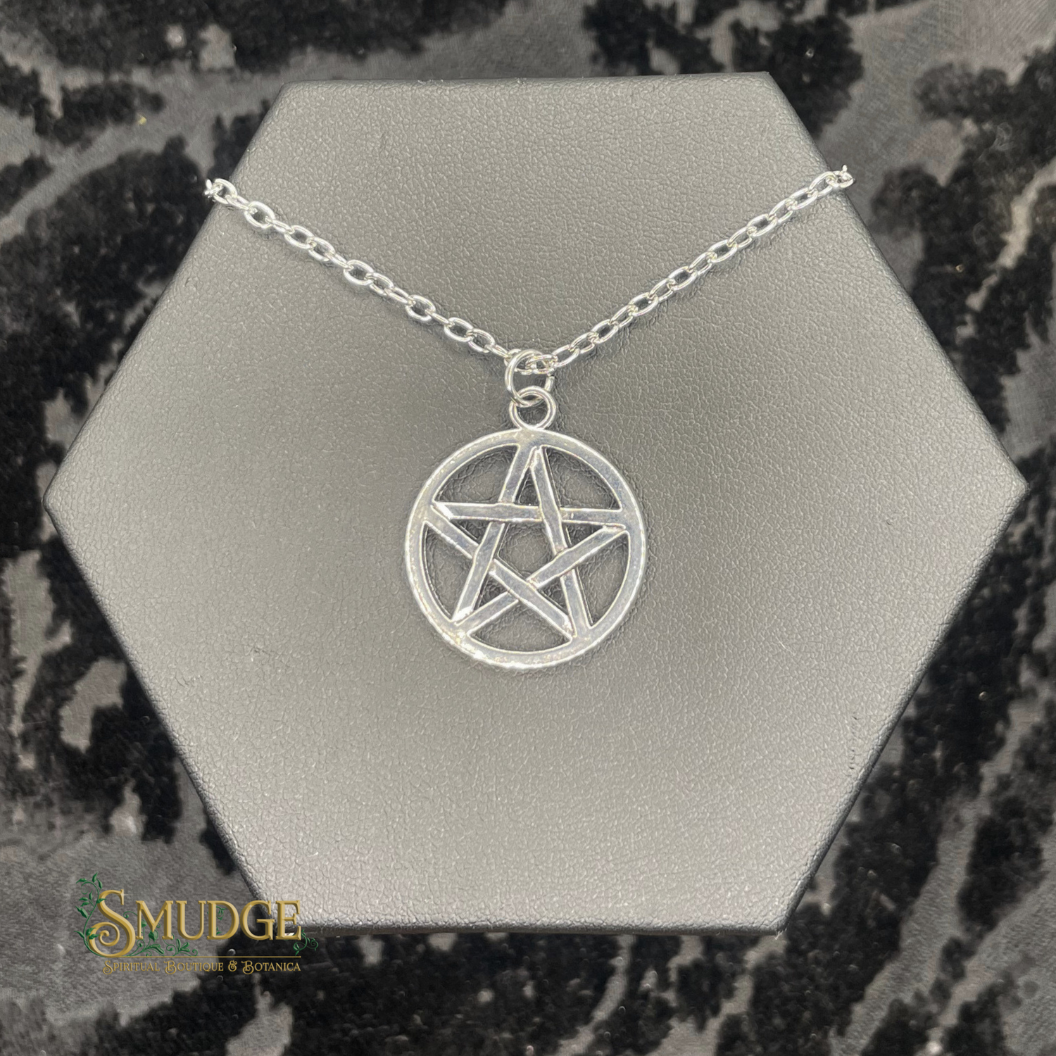 Silver pentagram necklace on a hexagonal silver stand with 'Smudge' branding.