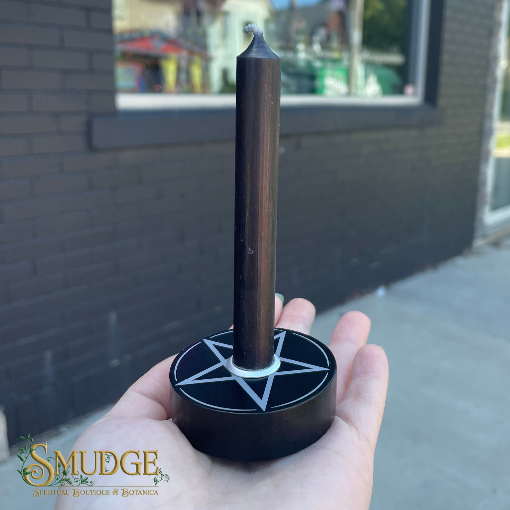Hand holding a black candle holder with pentagram design outdoors.