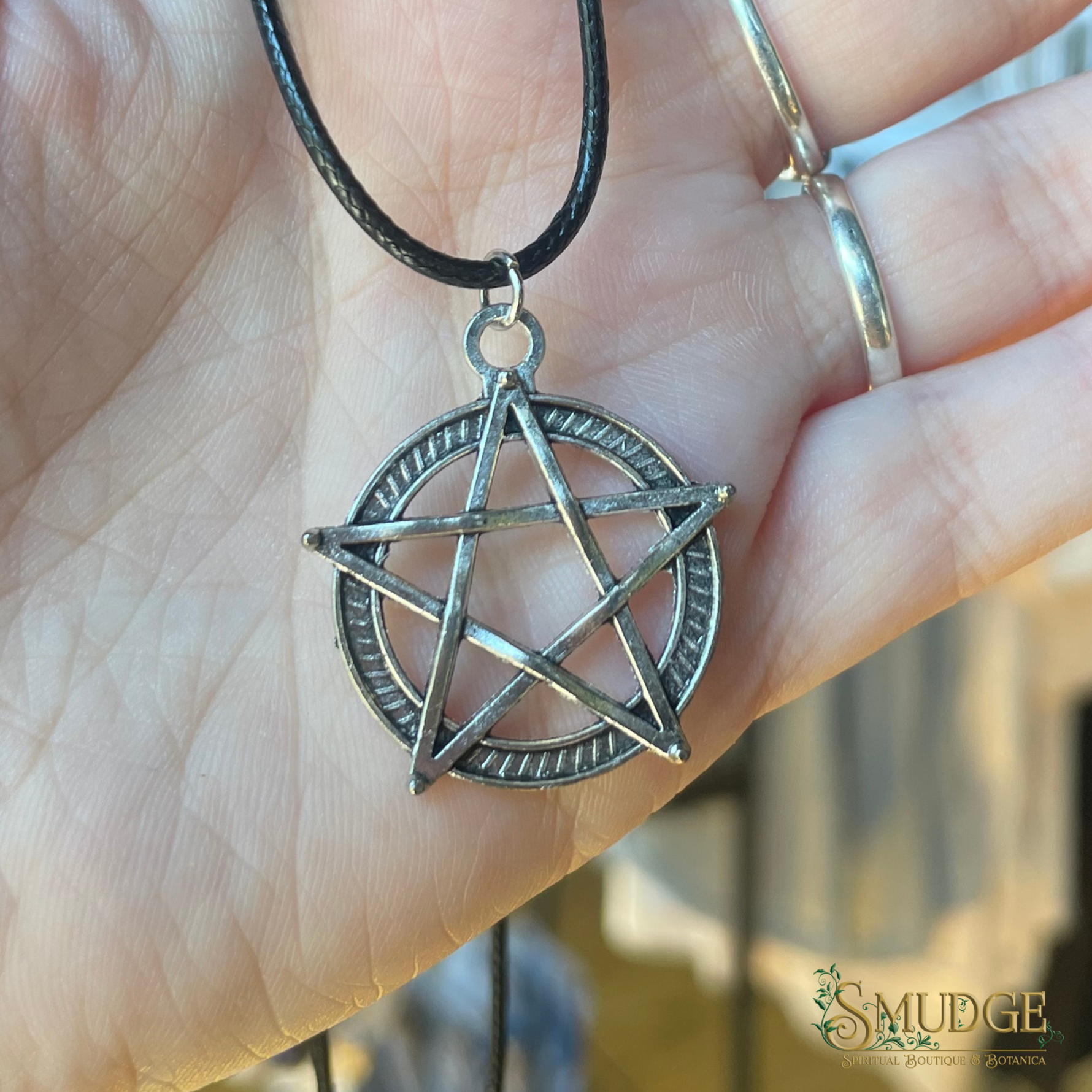 Silver pentagram pendant on a black cord held in a hand with a blurred background