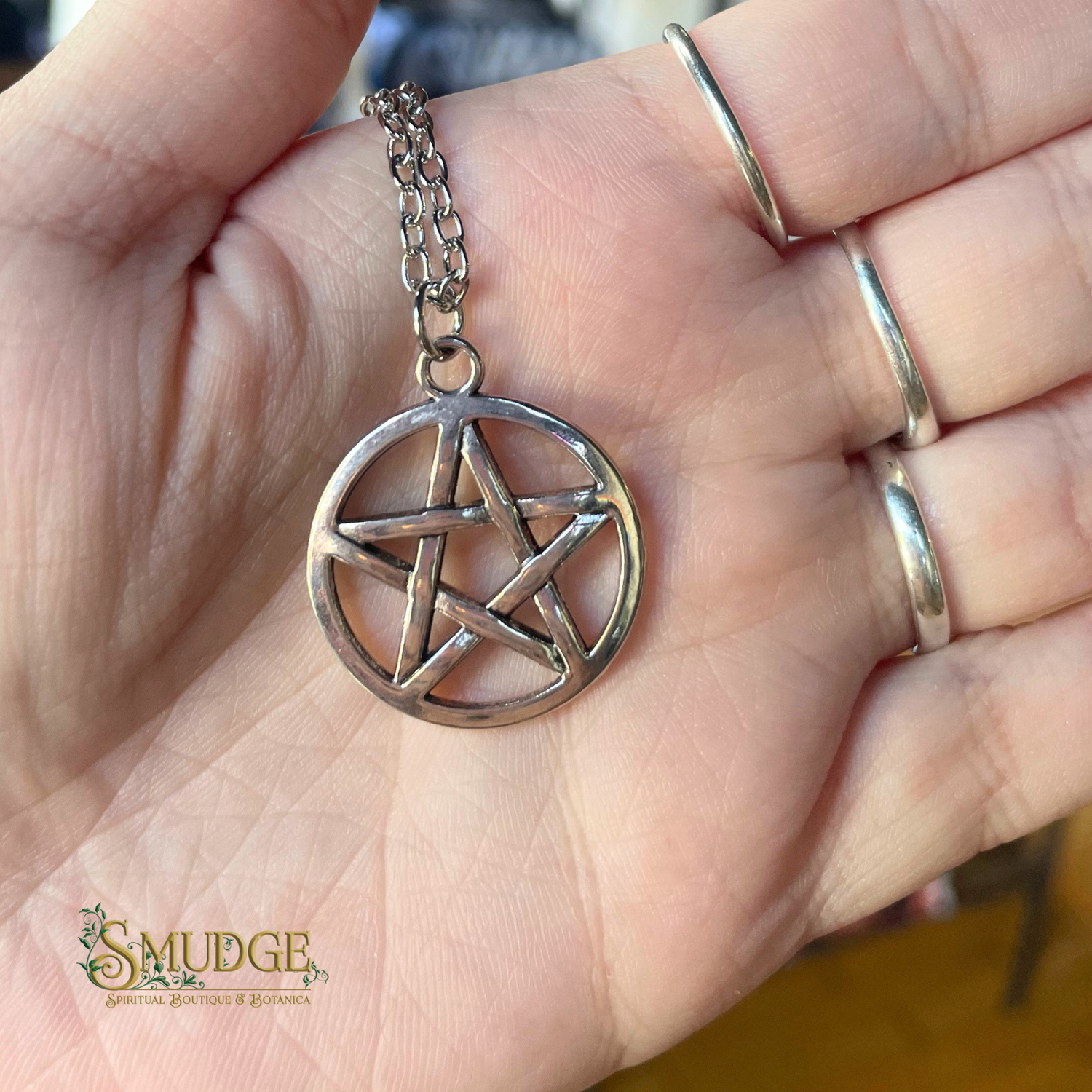 Silver pentagram pendant on a chain held in a hand with 'Smudge' branding.