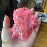 Pink crystal rock held in a hand with a blurred indoor background
