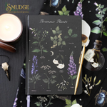 Notebook with botanical illustrations on a dark surface with a candle and pen.