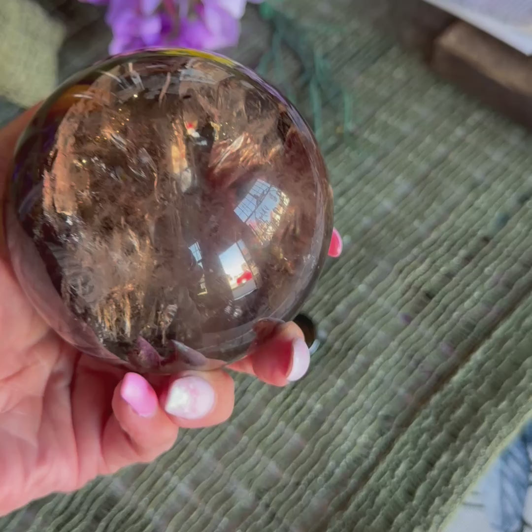 video of a smoky quartz large sphere with a hand turning it to see the colours.