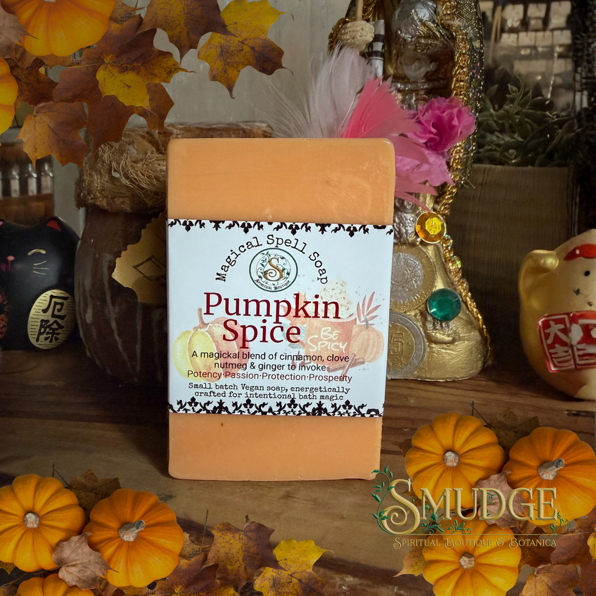 A rectangular bar of 'Pumpkin Spice' magical spell soap by Muzzy Spell Soap, featuring a white label with orange and black text. The soap is styled in a cozy autumn setting with small pumpkins, fall leaves, a cat, and a decorative boot in the background.