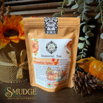 A stand-up pouch of Seasonal Tea Pumpkin Spice tea from Smudge Spiritual Boutique & Botanica, styled on a rustic wooden surface with autumn props including a sunflower, pinecone, and eucalyptus leaves.