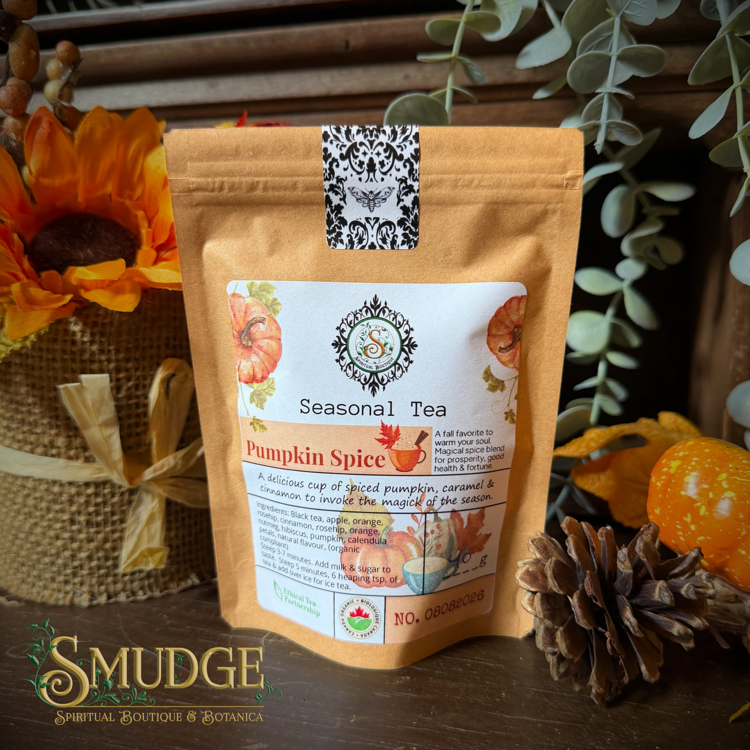 A stand-up pouch of Seasonal Tea Pumpkin Spice tea from Smudge Spiritual Boutique & Botanica, styled on a rustic wooden surface with autumn props including a sunflower, pinecone, and eucalyptus leaves.