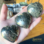 Three heart-shaped stones held in a hand with 'Smudge' brand logo in the corner.