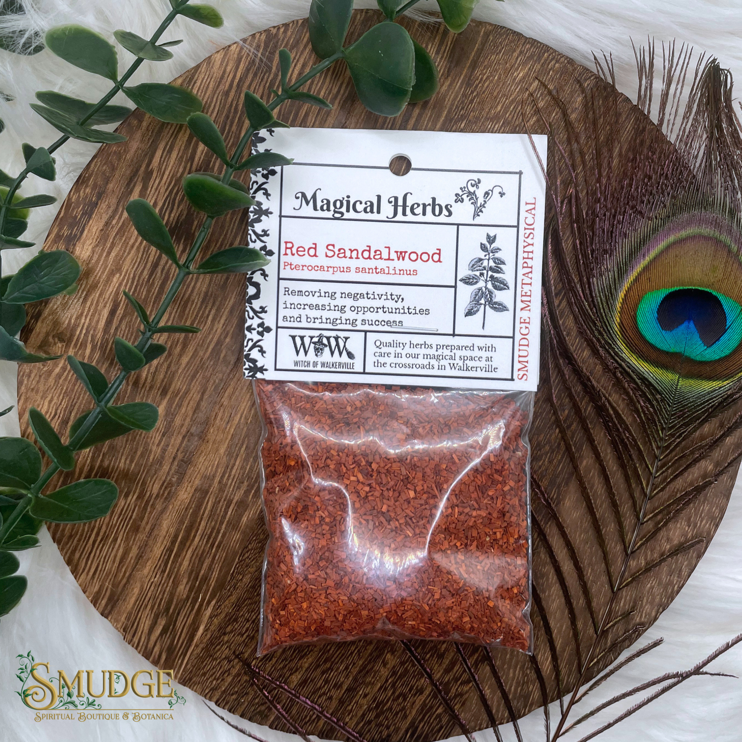 Bag of red sandalwood herbs with a label on a wooden board with peacock feather and greenery.