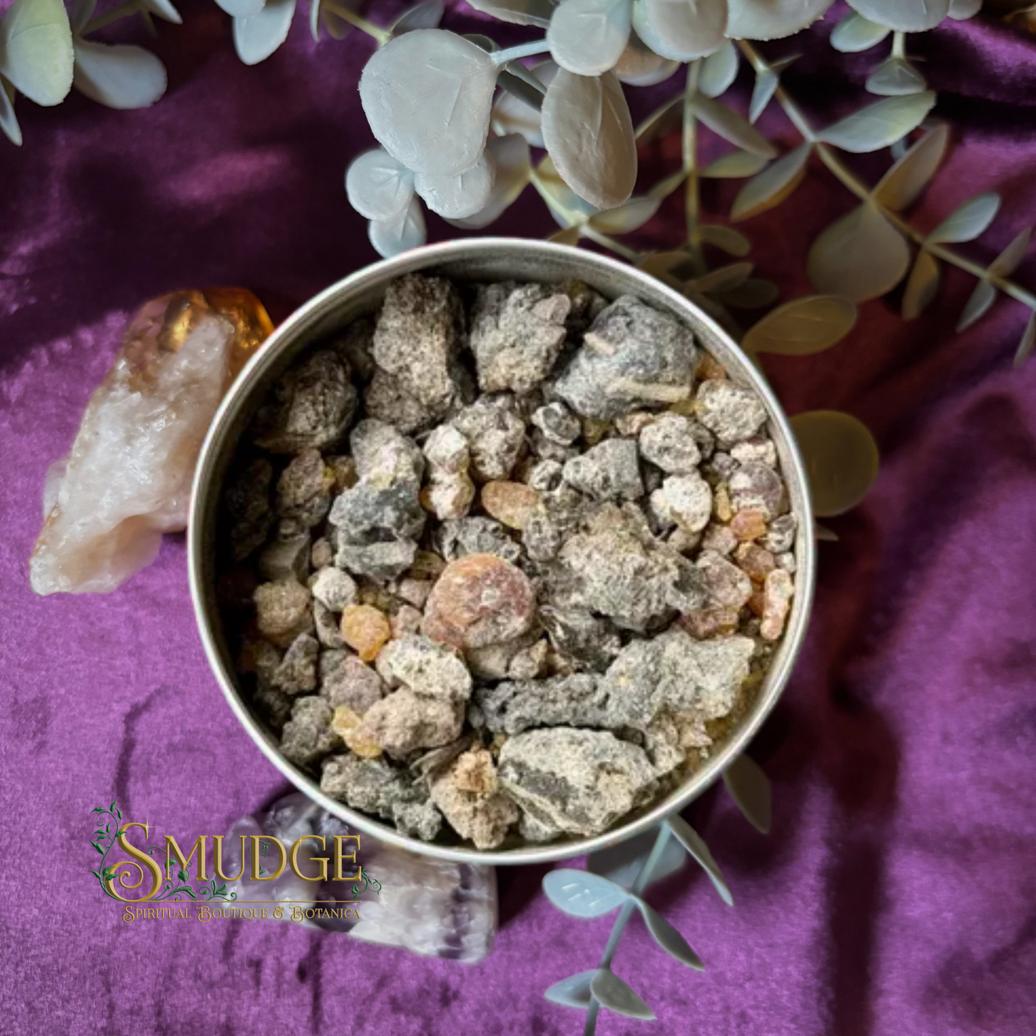 Metal container with palo santo resin incense on a purple fabric background with 'Smudge' branding.