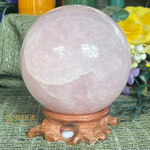 Rose quartz crystal sphere on a wooden stand with a blurred background
