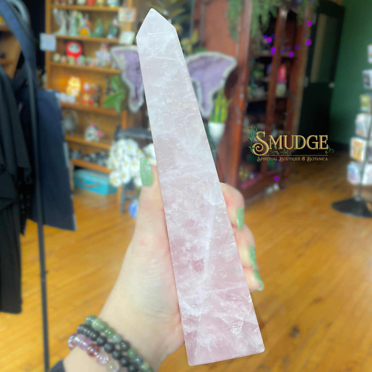Rose quartz crystal held by a hand with a blurred background featuring 'Smudge' brand name.