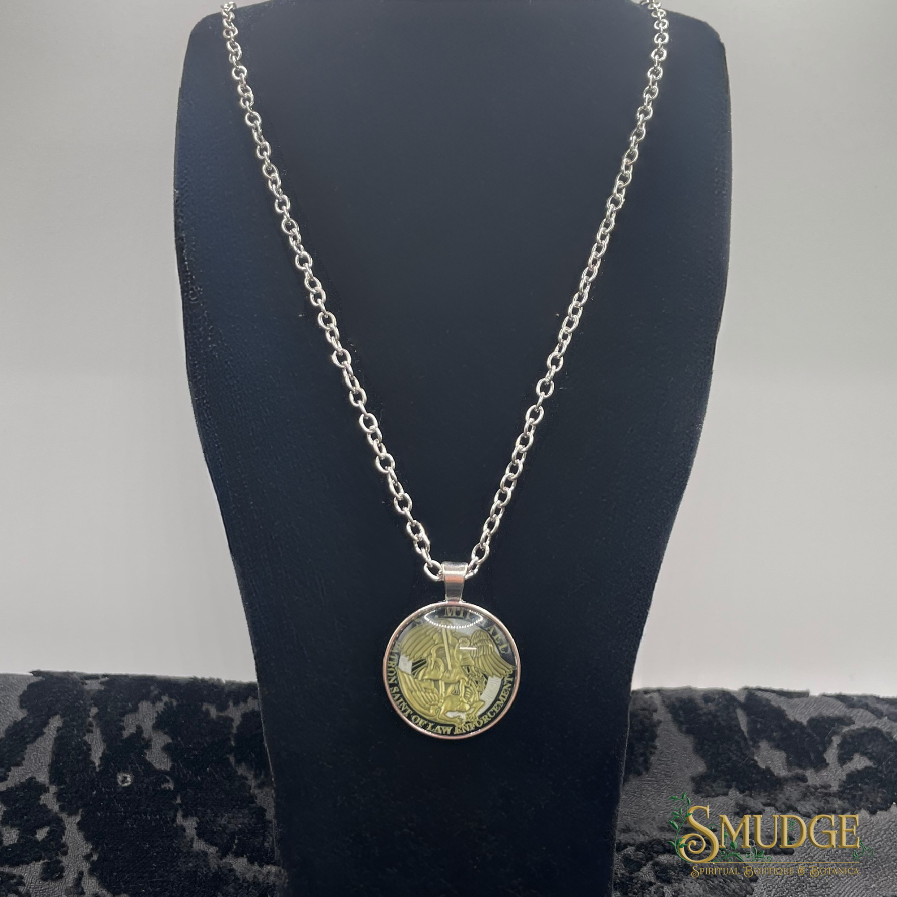 Silver chain necklace with a round pendant on a black mannequin bust.