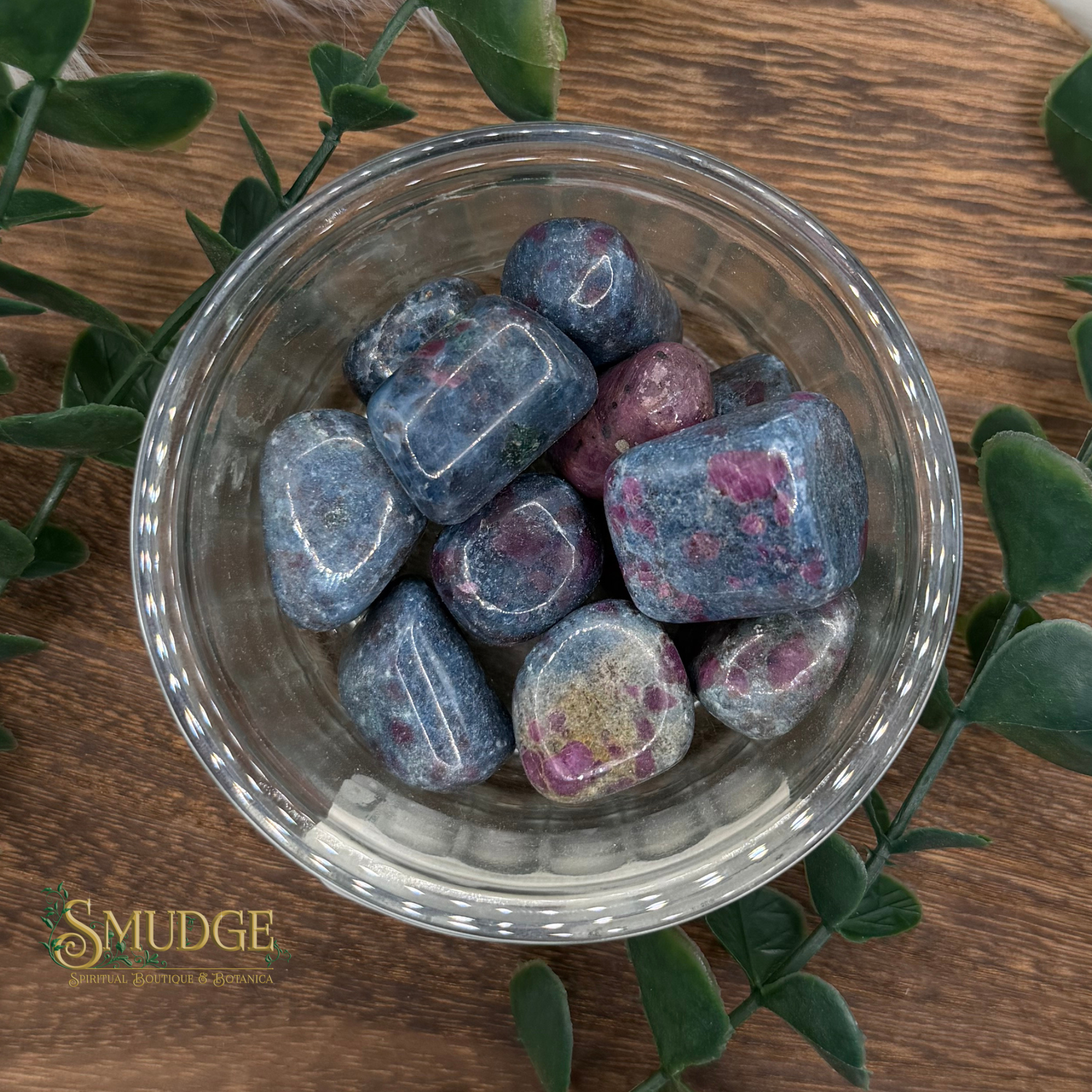 Clear glass bowl filled with colorful stones on a wooden surface with green leaves.