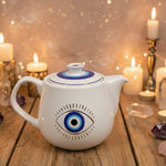 White teapot with blue eye design on a wooden surface