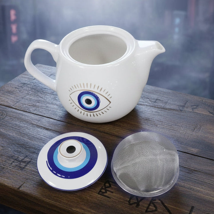 White teapot with evil eye design, lid, and metal filter on a white background