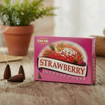 Pink box of strawberry incense cones with smoke and plants in the background