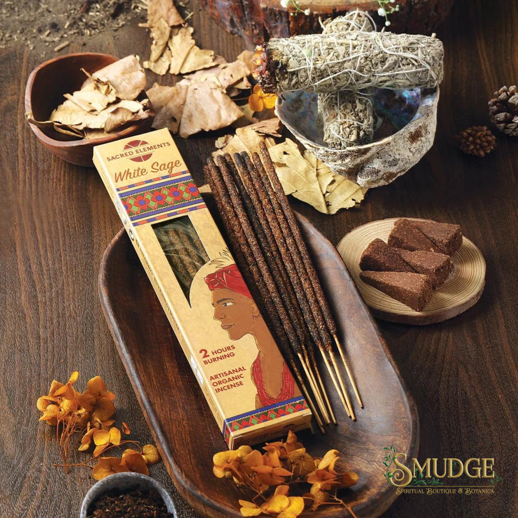 White Sage smudge sticks with packaging on a wooden tray, surrounded by dried herbs and elements.