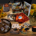 A styled tabletop display of a Salem Oracle card deck set, including the main 'Seasons of the Witch' box, two card decks, several individual cards, a candle jar labeled Mabon, crystals on a wooden tray, yellow flowers, and lit candles on a wooden surface.