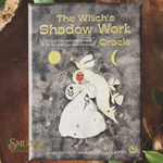 The Witch's Shadow Work Oracle card deck box by Smudge, featuring a dark textured cover with a white rabbit, yellow moon and sun, and gold lettering, photographed on a rustic wood surface.