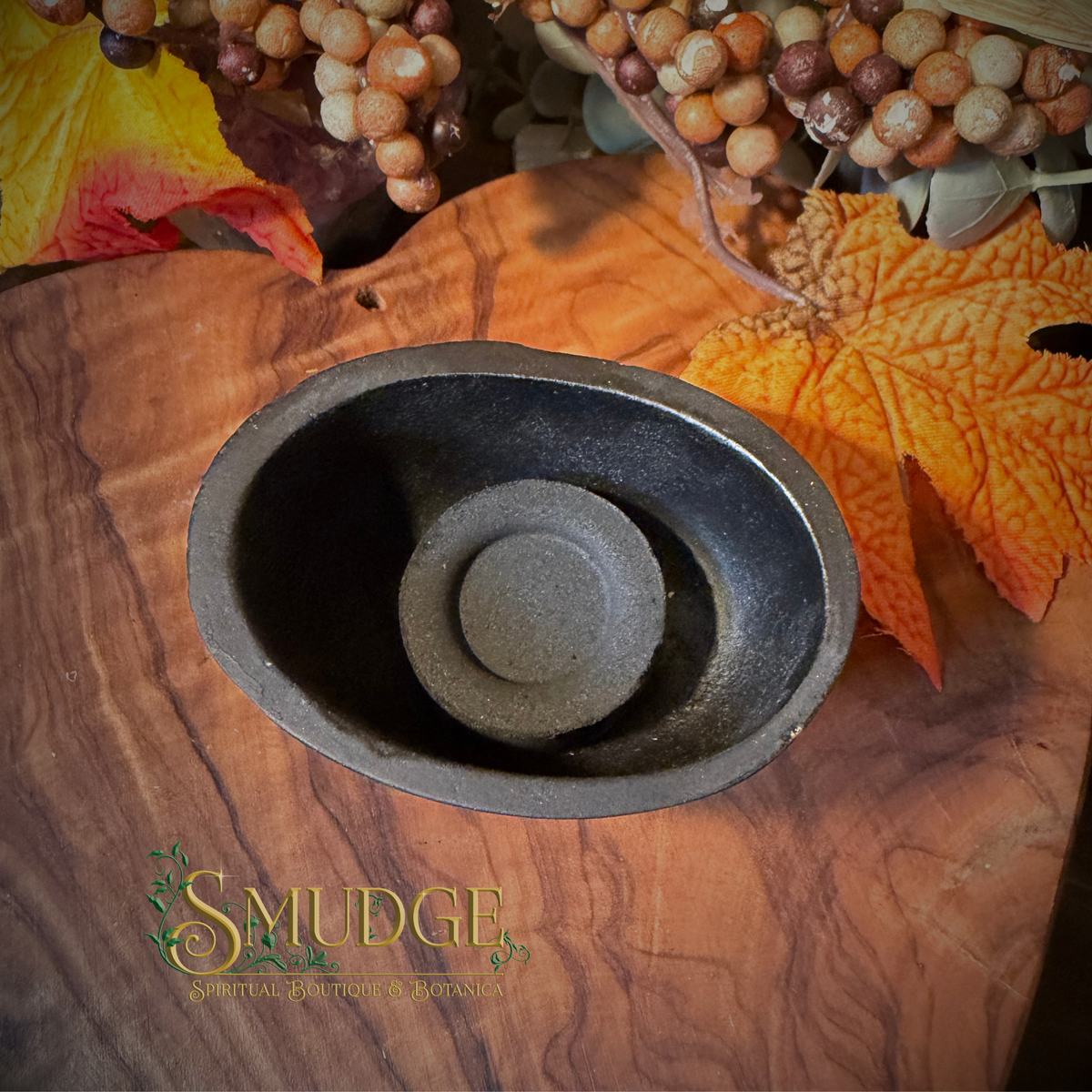 A dark gray ceramic or stone candle holder with a textured finish, displayed on a rustic wooden board decorated with autumn leaves and grapevine accents. The brand name 'SMUDGE' is visible in the bottom-left corner.