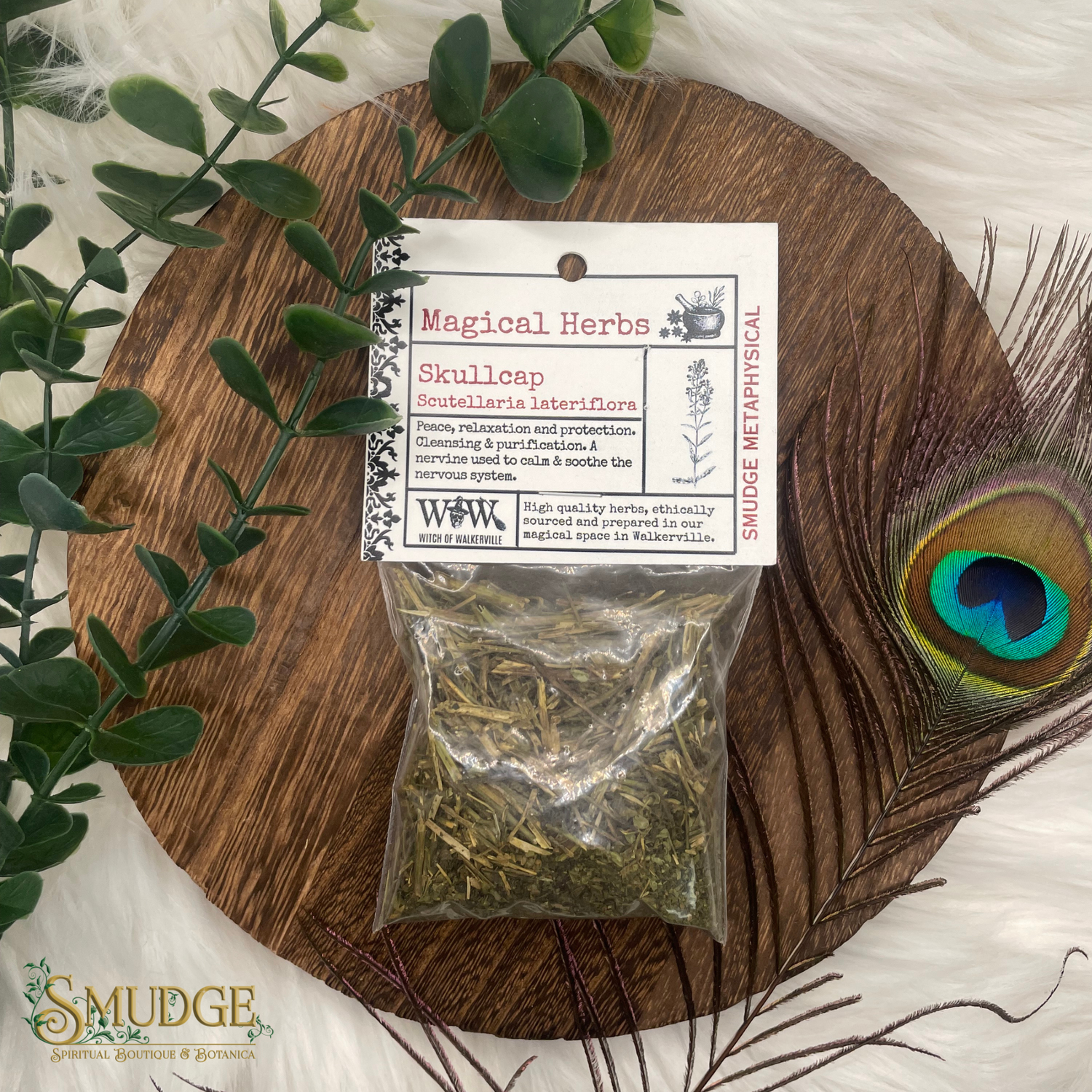 Bag of skullcap herbs on a wooden board with a peacock feather and eucalyptus leaves.