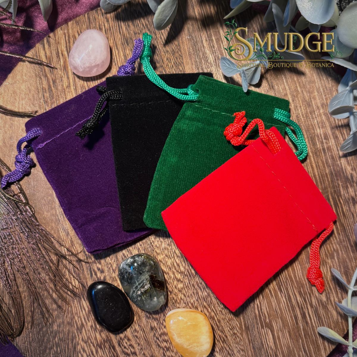 Four velvet bags in purple, black, green, and red on a wooden surface with crystals.