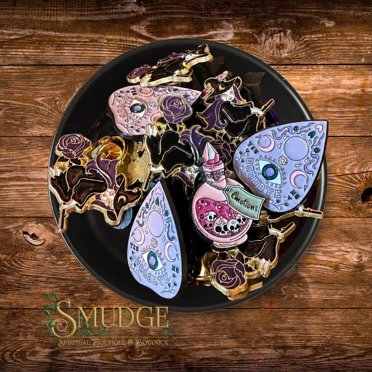 A collection of decorative, handcrafted resin jewelry pieces displayed on a black plate over a rustic wooden background. The jewelry features intricate designs including a rose, a teardrop with a moon and star motif, and a small pink teardrop with a label reading 'Cruelty'.