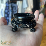 Black ornate incense holder held in a hand with a blurred background