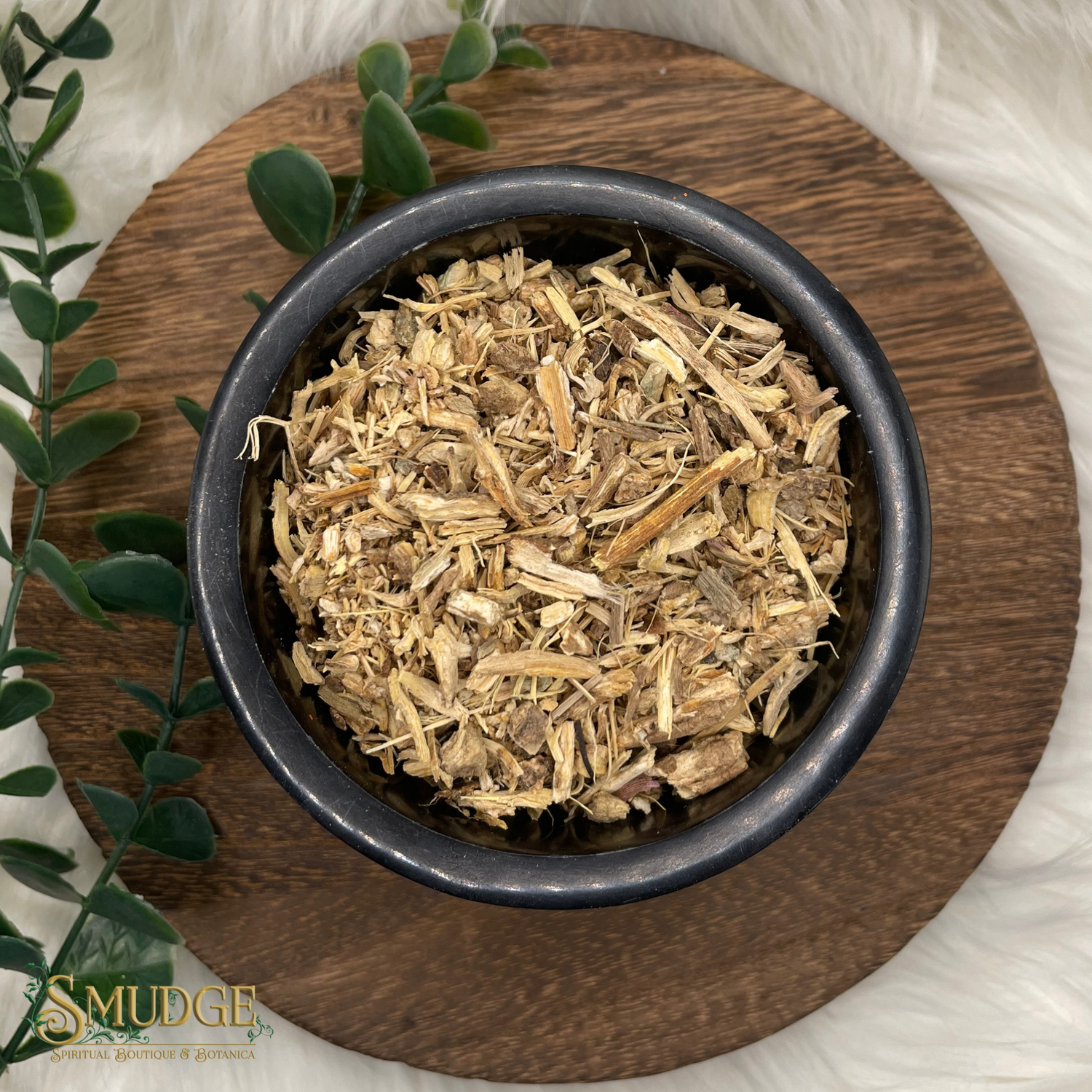Dried herbs in a black bowl on a wooden surface with a plant in the background