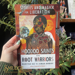Book titled 'Stories and Magick for Liberation: Hoodoo Saints and Root Warriors' held by a hand with green nail polish, surrounded by plants.