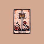 A tarot card illustration titled 'THE SUN' centered on a solid tan background. The card shows a vertical sword with a radiant sunburst at the hilt, red flowers, and a peach-toned watercolor background.