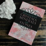 Book titled 'The Essential Guide to Crystals, Minerals and Stones' by Margaret Ann Lembo on a wooden surface with crystals.
