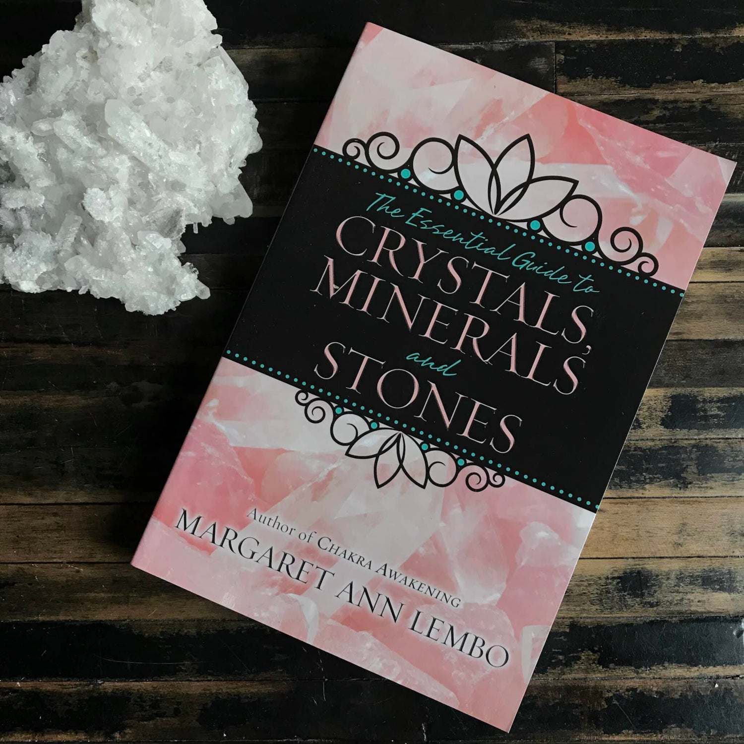 Book titled 'The Essential Guide to Crystals, Minerals and Stones' by Margaret Ann Lembo on a wooden surface with crystals.